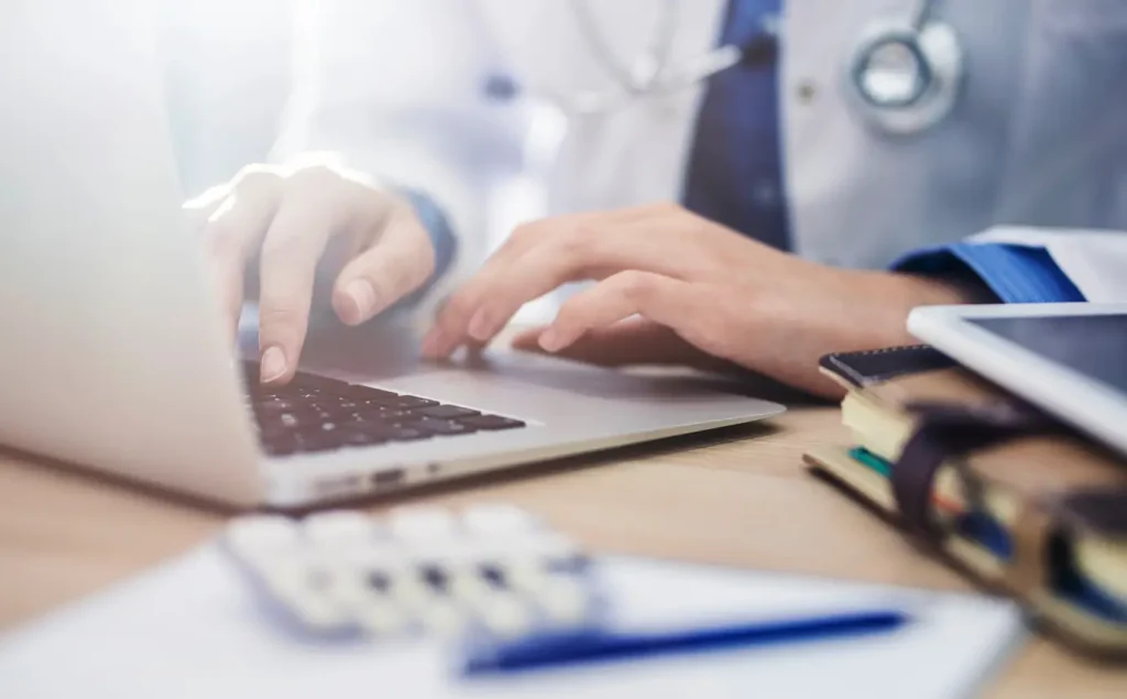 A doctor typing on a laptop, focused on their work in a clinical setting.