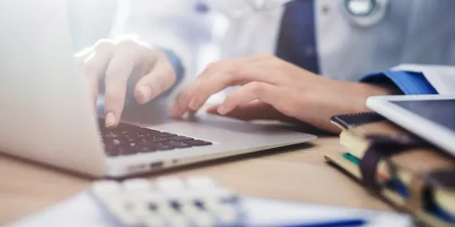 A doctor typing on a laptop, focused on their work in a clinical setting.