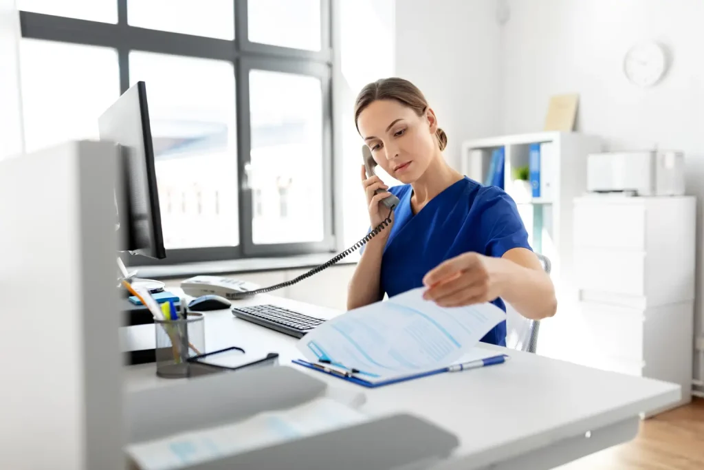 A woman in blue scrubs is speaking on the phone, appearing engaged in a conversation.