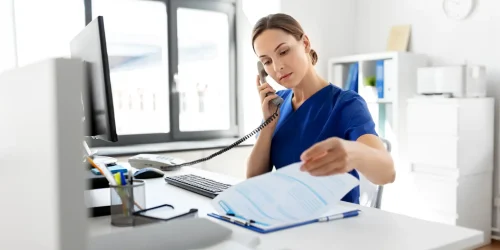 A woman in blue scrubs is speaking on the phone, appearing engaged in a conversation.