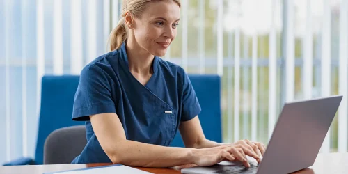 a female healthcare professional sitting at a desk and typing on a laptop