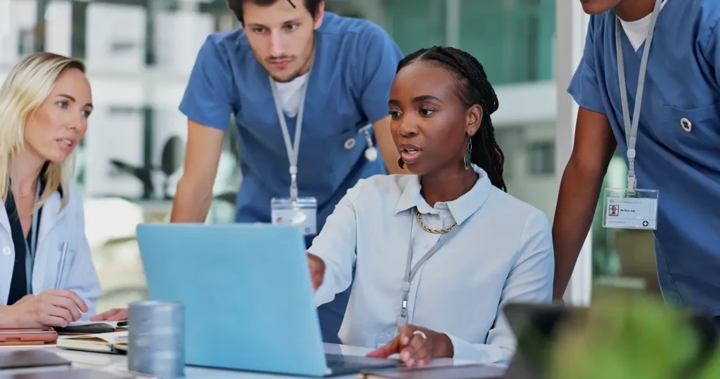 A group of doctors and nurses collaborating on a laptop in a medical setting, focused on their task.