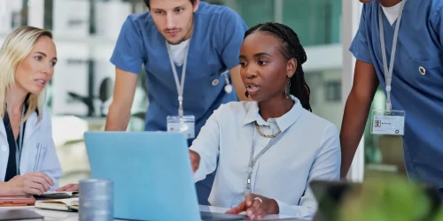 A group of doctors and nurses collaborating on a laptop in a medical setting, focused on their task.